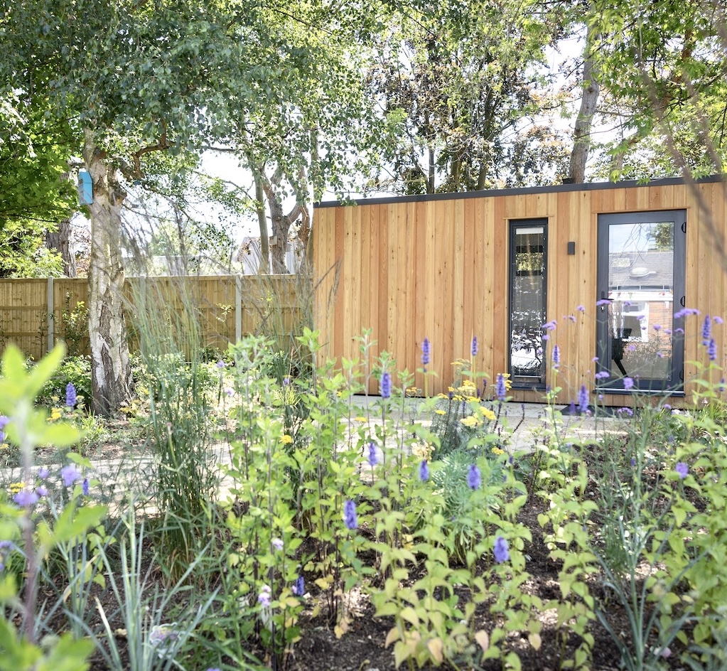 Timber garden room among mature trees with flowering perennial planting in the foreground
