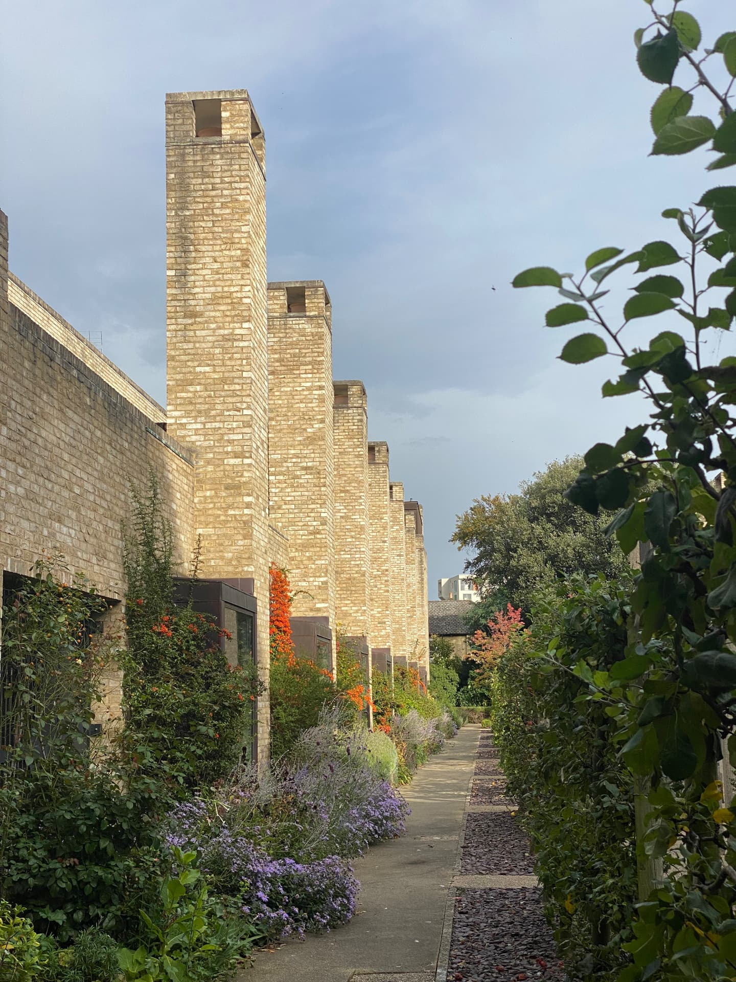 Stepped brick chimneys above a planted path in late afternoon light